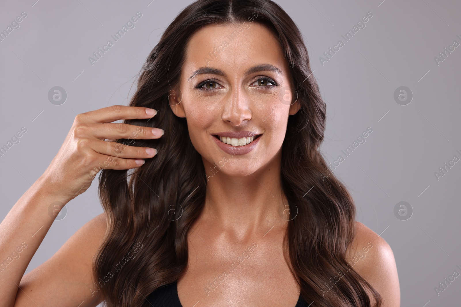 Photo of Hair styling. Portrait of beautiful woman with wavy long hair on grey background, closeup