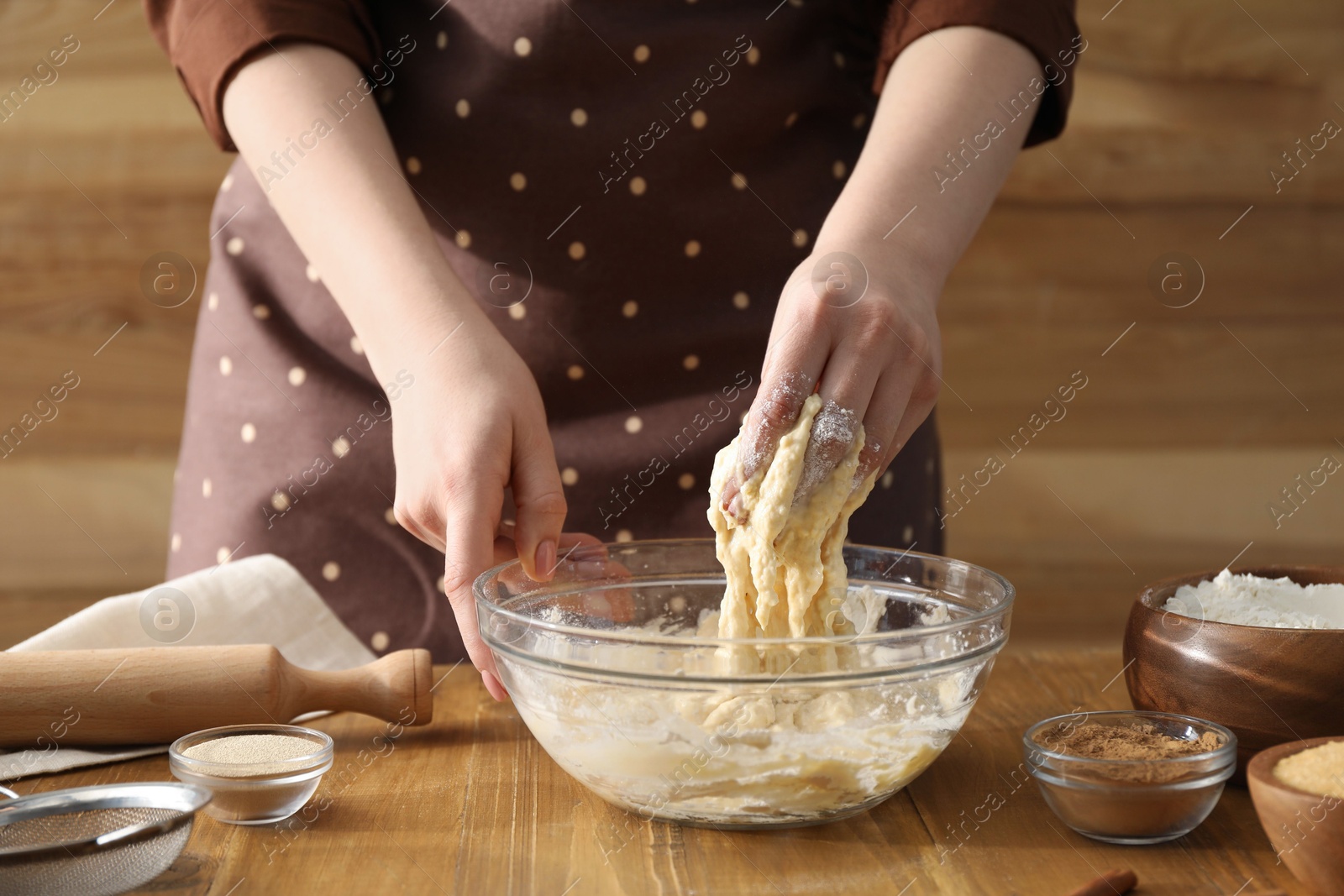 Photo of Woman kneading dough for cinnamon rolls at wooden table, closeup