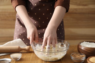 Photo of Woman kneading dough for cinnamon rolls at wooden table, closeup