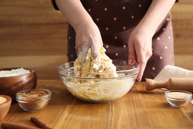 Photo of Woman kneading dough for cinnamon rolls at wooden table, closeup