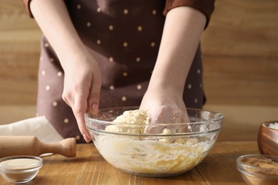 Photo of Woman kneading dough for cinnamon rolls at wooden table, closeup