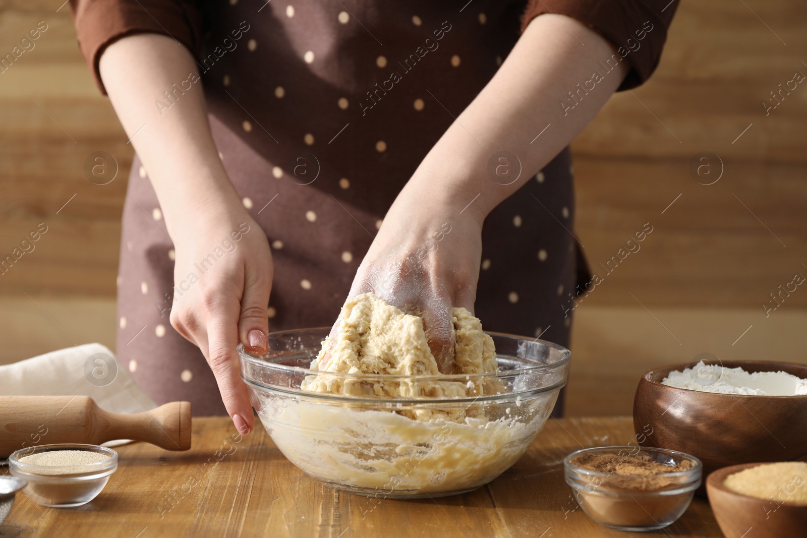 Photo of Woman kneading dough for cinnamon rolls at wooden table, closeup