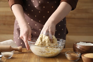 Photo of Woman kneading dough for cinnamon rolls at wooden table, closeup