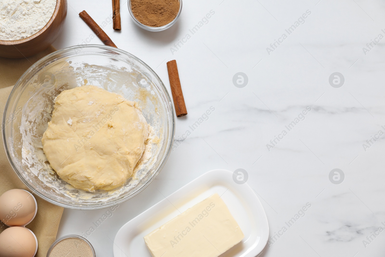 Photo of Making cinnamon rolls. Fresh dough in bowl and ingredients on white marble table, flat lay. Space for text