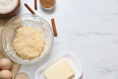 Photo of Making cinnamon rolls. Fresh dough in bowl and ingredients on white marble table, flat lay. Space for text