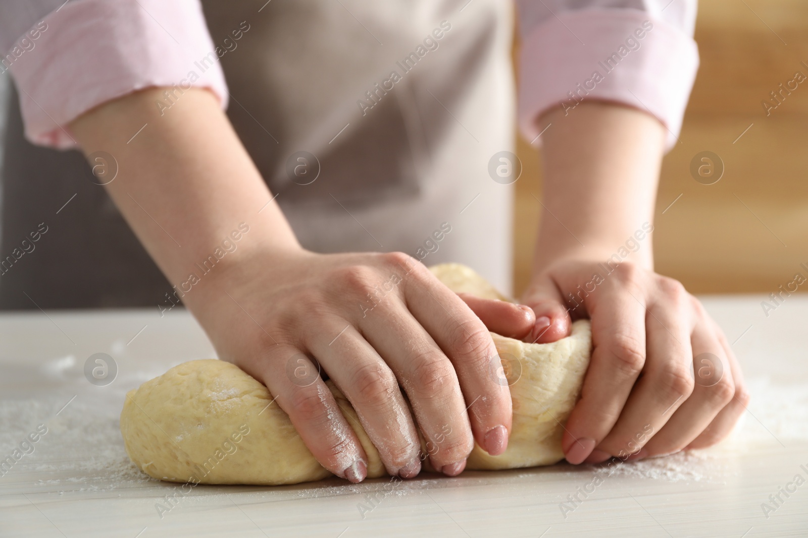 Photo of Woman kneading dough for cinnamon rolls at white table, closeup