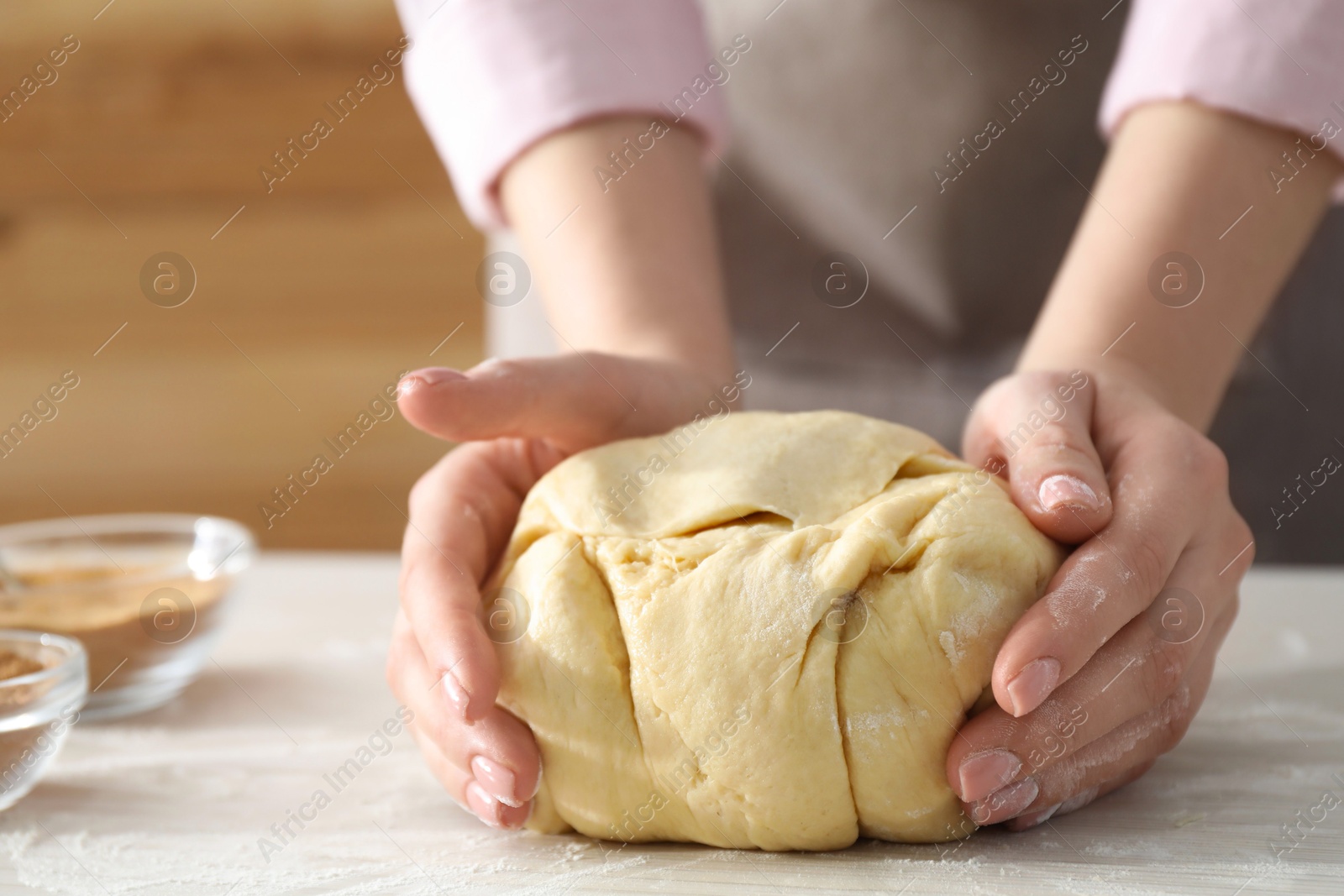 Photo of Woman kneading dough for cinnamon rolls at white table, closeup