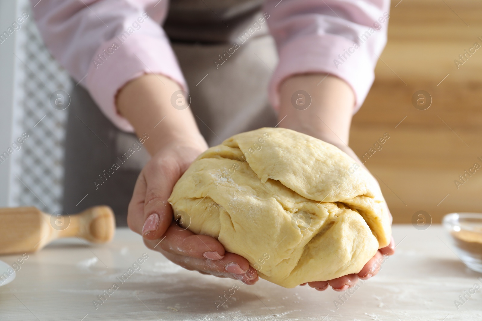 Photo of Woman kneading dough for cinnamon rolls at white table, closeup