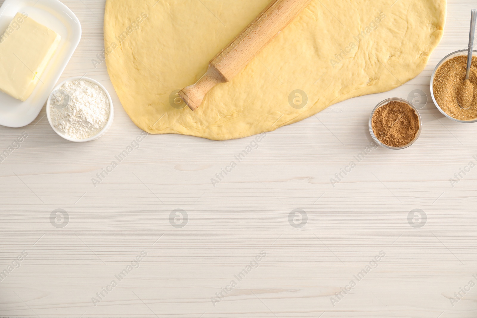 Photo of Making cinnamon rolls. Dough, other ingredients and rolling pin on white wooden table, flat lay. Space for text