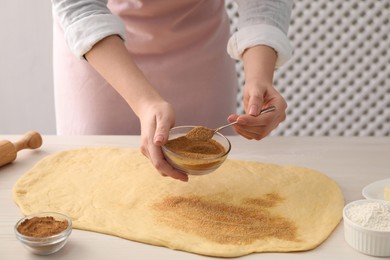 Photo of Making cinnamon rolls. Woman adding spice with sugar into dough at white wooden table, closeup