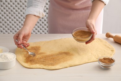 Photo of Making cinnamon rolls. Woman adding spice with sugar into dough at white wooden table, closeup