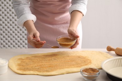 Photo of Making cinnamon rolls. Woman adding spice with sugar into dough at white wooden table, closeup