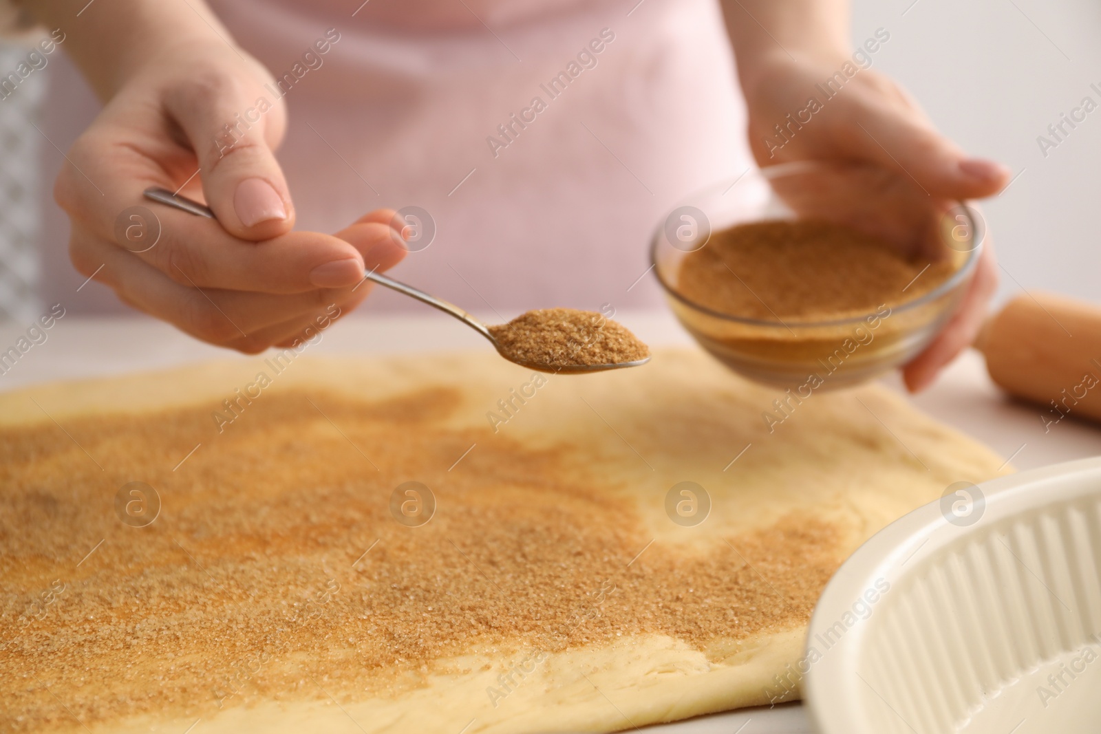 Photo of Making cinnamon rolls. Woman adding spice with sugar into dough at table, closeup