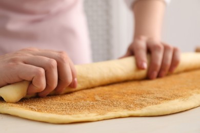 Photo of Making cinnamon rolls. Woman shaping dough at white table, closeup