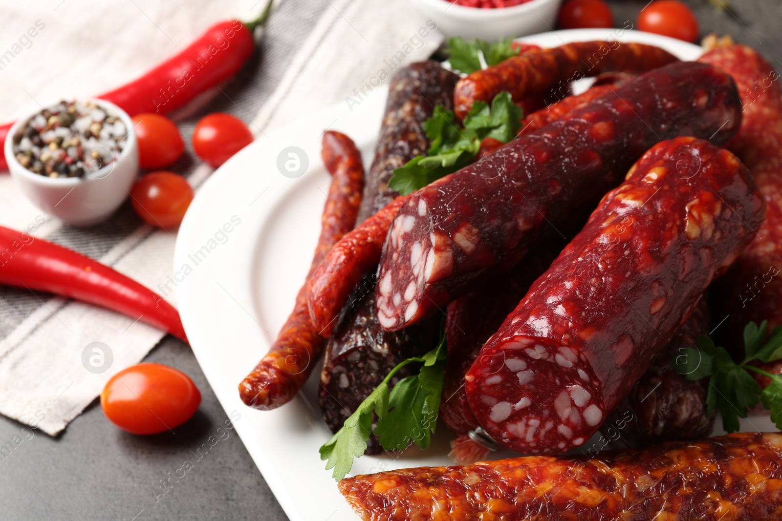 Photo of Different smoked sausages, parsley, spices and products on grey table, closeup