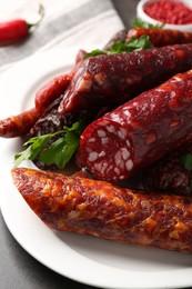 Photo of Different smoked sausages and parsley on grey table, closeup