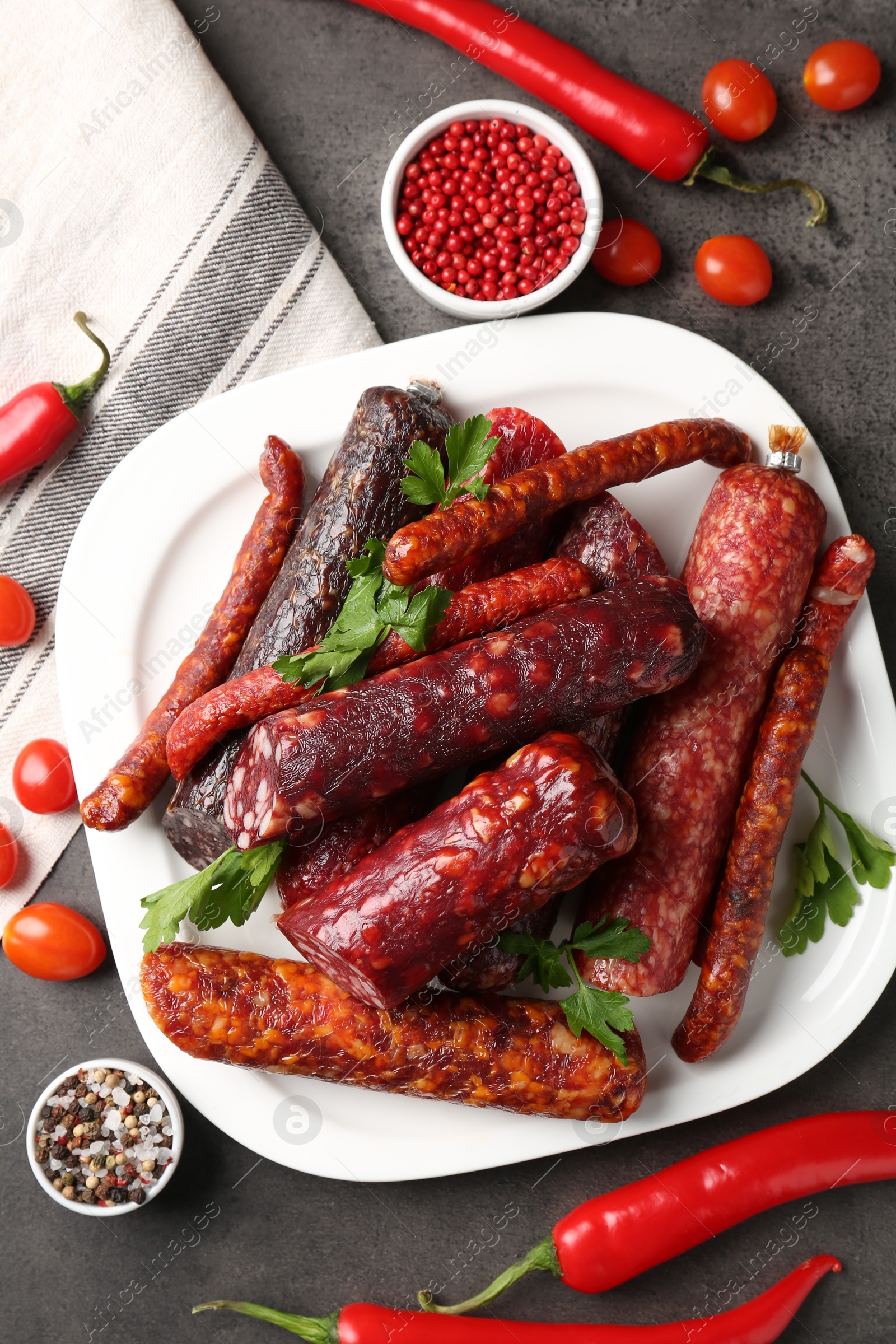 Photo of Flat lay composition with different smoked sausages and peppercorns on grey textured table