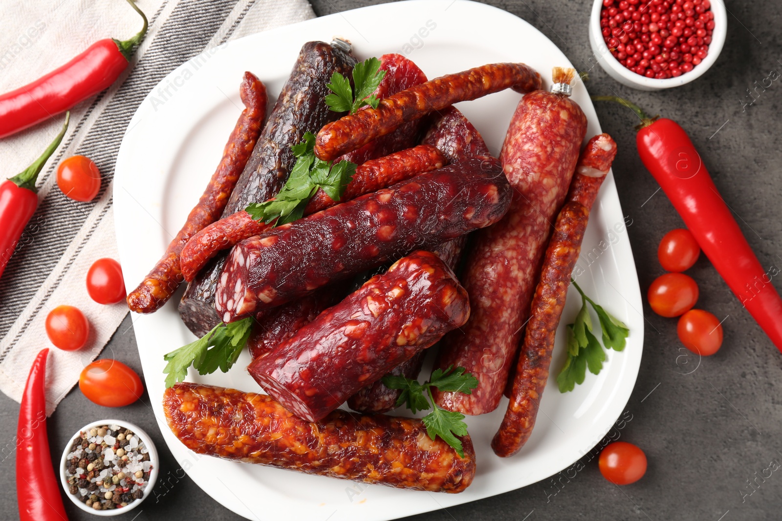 Photo of Flat lay composition with different smoked sausages and peppercorns on grey textured table