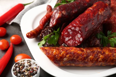 Photo of Different smoked sausages, parsley, peppercorns, tomatoes and chili pepper on grey textured table, closeup