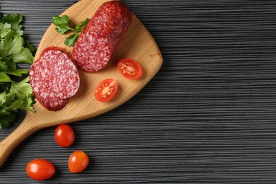 Photo of Cut smoked sausage, tomatoes and parsley on black wooden table, flat lay. Space for text