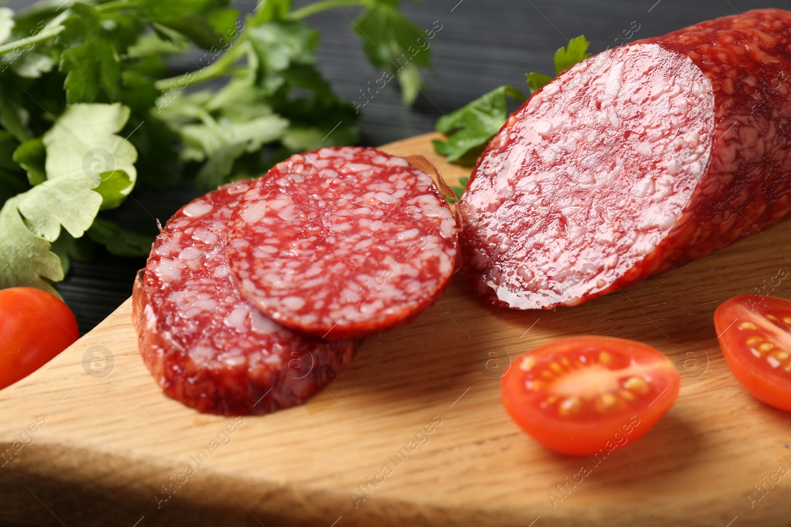 Photo of Cut smoked sausage, tomato and parsley on black table, closeup