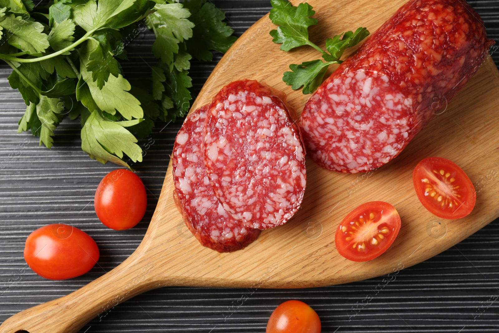 Photo of Cut smoked sausage, tomatoes and parsley on black wooden table, flat lay