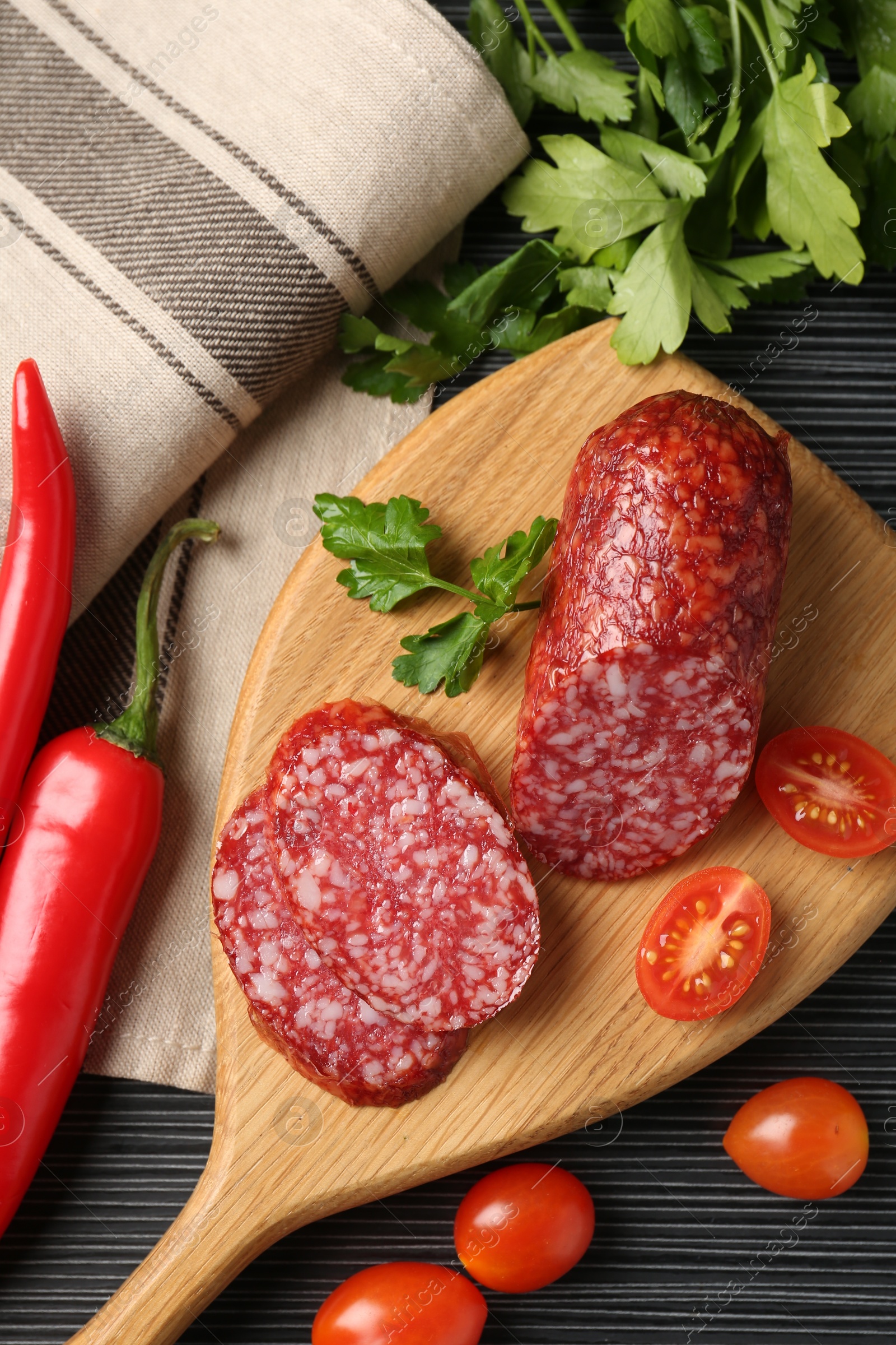 Photo of Cut smoked sausage, parsley, tomatoes and chili pepper on black wooden table, flat lay