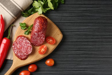 Photo of Cut smoked sausage, parsley, tomatoes and chili pepper on black wooden table, flat lay. Space for text