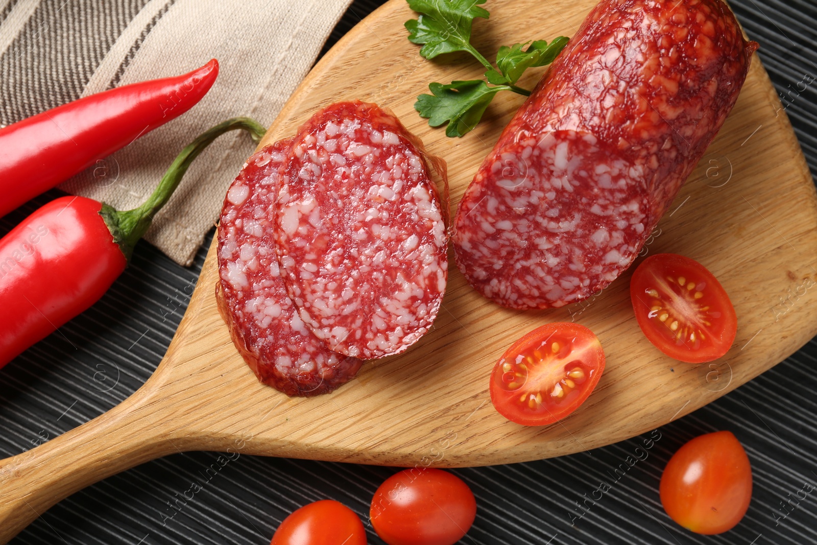 Photo of Cut smoked sausage, parsley, tomatoes and chili pepper on black wooden table, flat lay