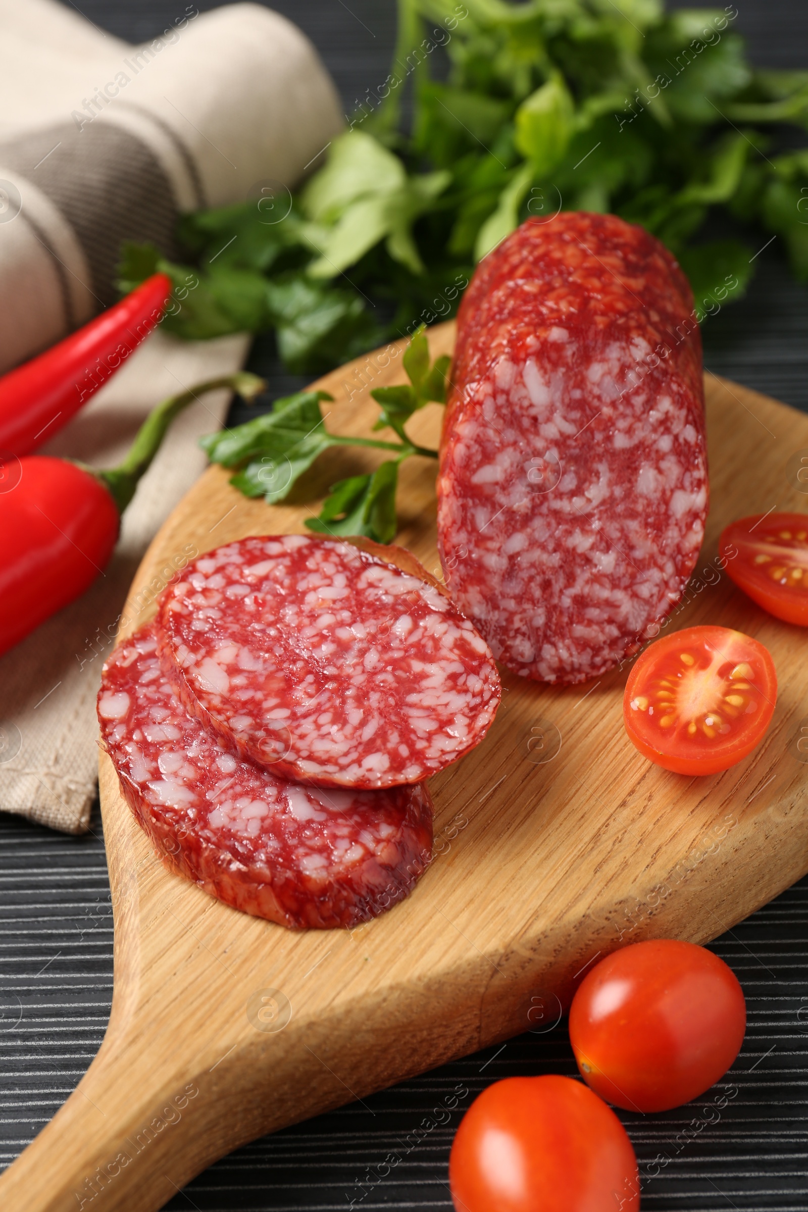 Photo of Cut smoked sausage, parsley, tomatoes and chili pepper on black wooden table, closeup