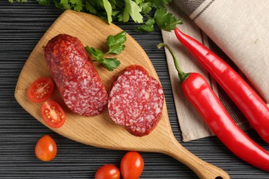 Photo of Cut smoked sausage, parsley, tomatoes and chili pepper on black wooden table, flat lay