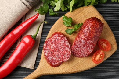 Photo of Cut smoked sausage, parsley, tomatoes and chili pepper on black wooden table, flat lay