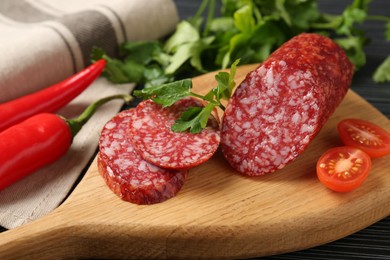 Photo of Cut smoked sausage, parsley and tomatoes on black wooden table, closeup