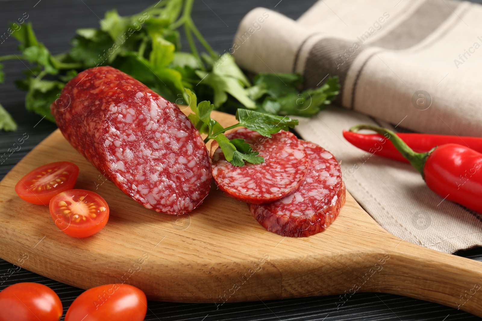 Photo of Cut smoked sausage, parsley and tomatoes on black wooden table, closeup