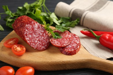 Photo of Cut smoked sausage, parsley and tomatoes on black wooden table, closeup