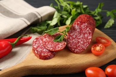 Photo of Cut smoked sausage, parsley and tomatoes on black wooden table, closeup