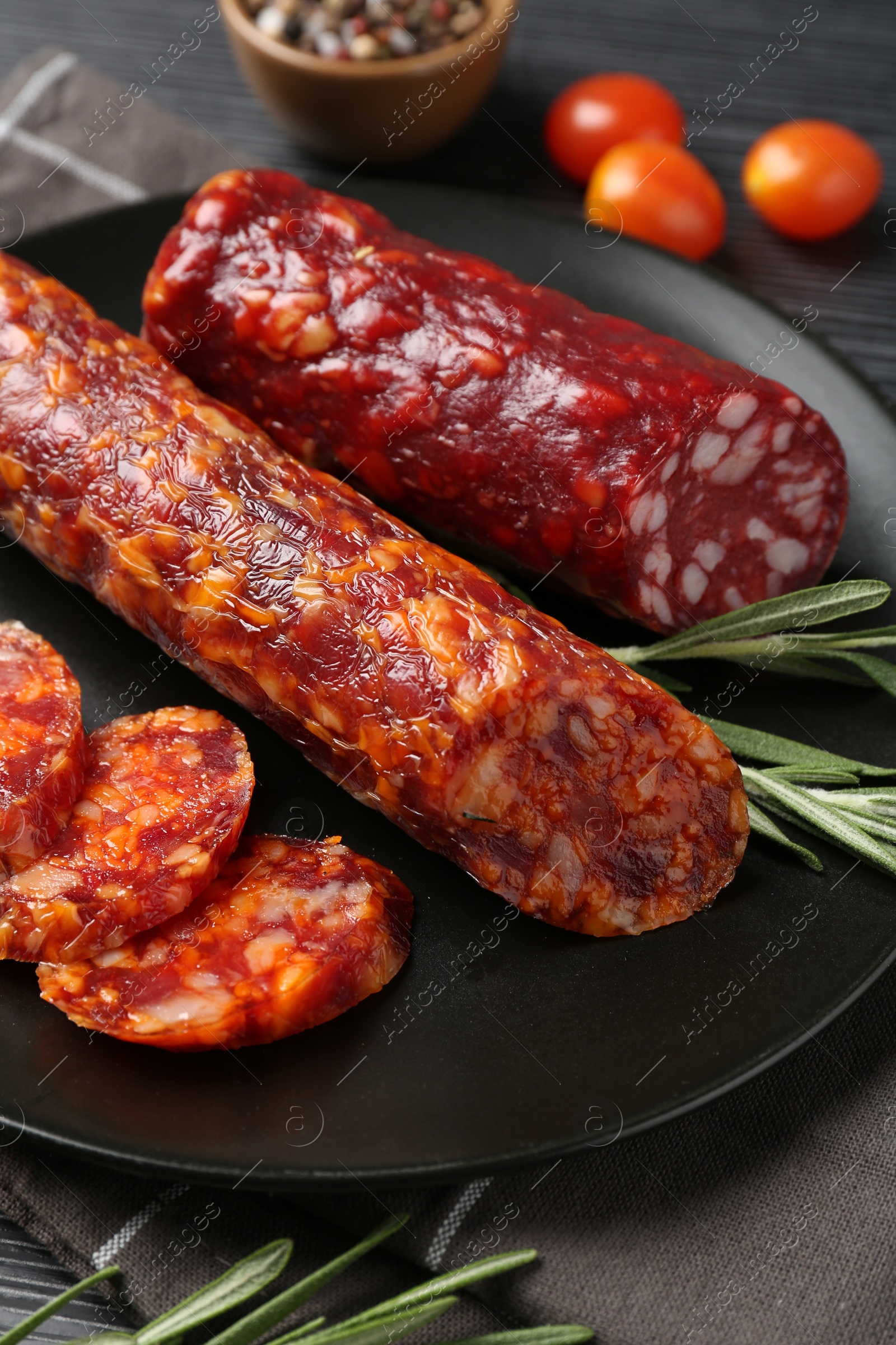 Photo of Cut smoked sausages, rosemary and tomatoes on black table, closeup