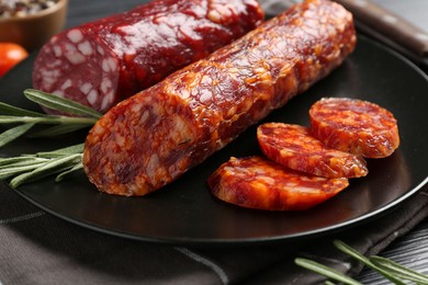 Photo of Cut smoked sausages, rosemary and tomatoes on black table, closeup