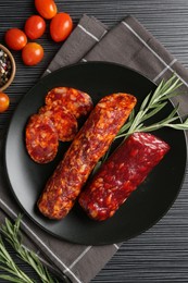 Photo of Cut smoked sausages, rosemary and tomatoes on black wooden table, flat lay