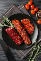 Photo of Cut smoked sausages, rosemary and tomatoes on black wooden table, flat lay