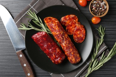 Photo of Cut smoked sausages, rosemary, peppercorns and tomatoes on black wooden table, flat lay