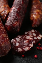 Photo of Different smoked sausages and peppercorns on black table, closeup