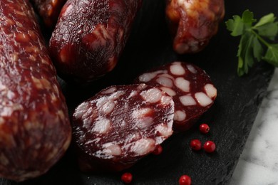 Photo of Different smoked sausages and peppercorns on light table, closeup