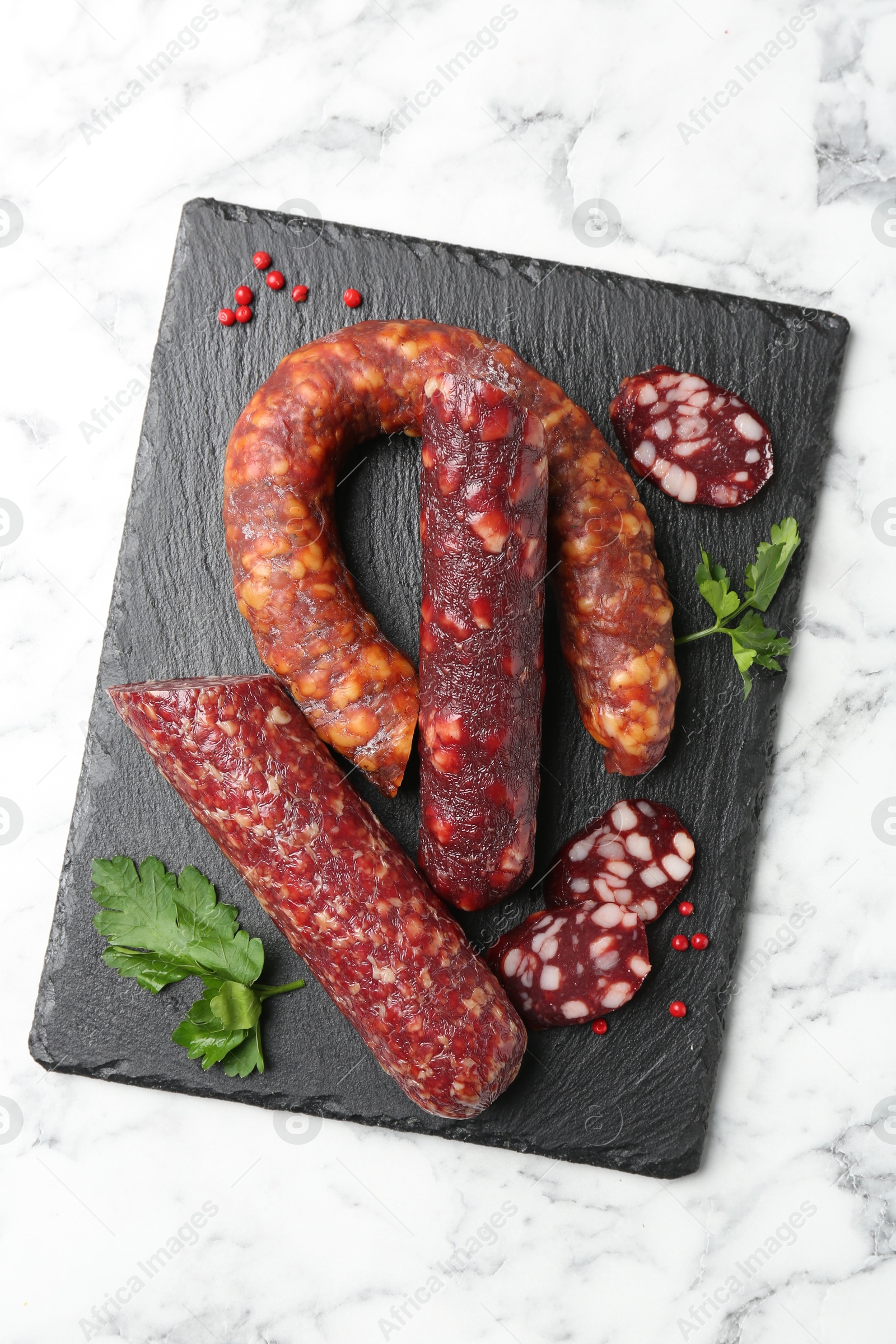 Photo of Different smoked sausages, parsley and peppercorns on white marble table, top view