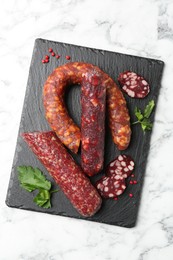 Photo of Different smoked sausages, parsley and peppercorns on white marble table, top view