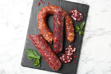 Photo of Different smoked sausages, parsley and peppercorns on white marble table, top view