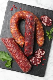 Photo of Different smoked sausages, parsley and peppercorns on white marble table, top view