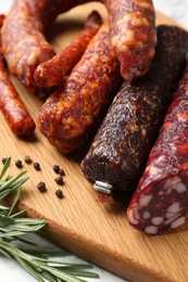 Photo of Different smoked sausages, rosemary and peppercorns on white table, closeup