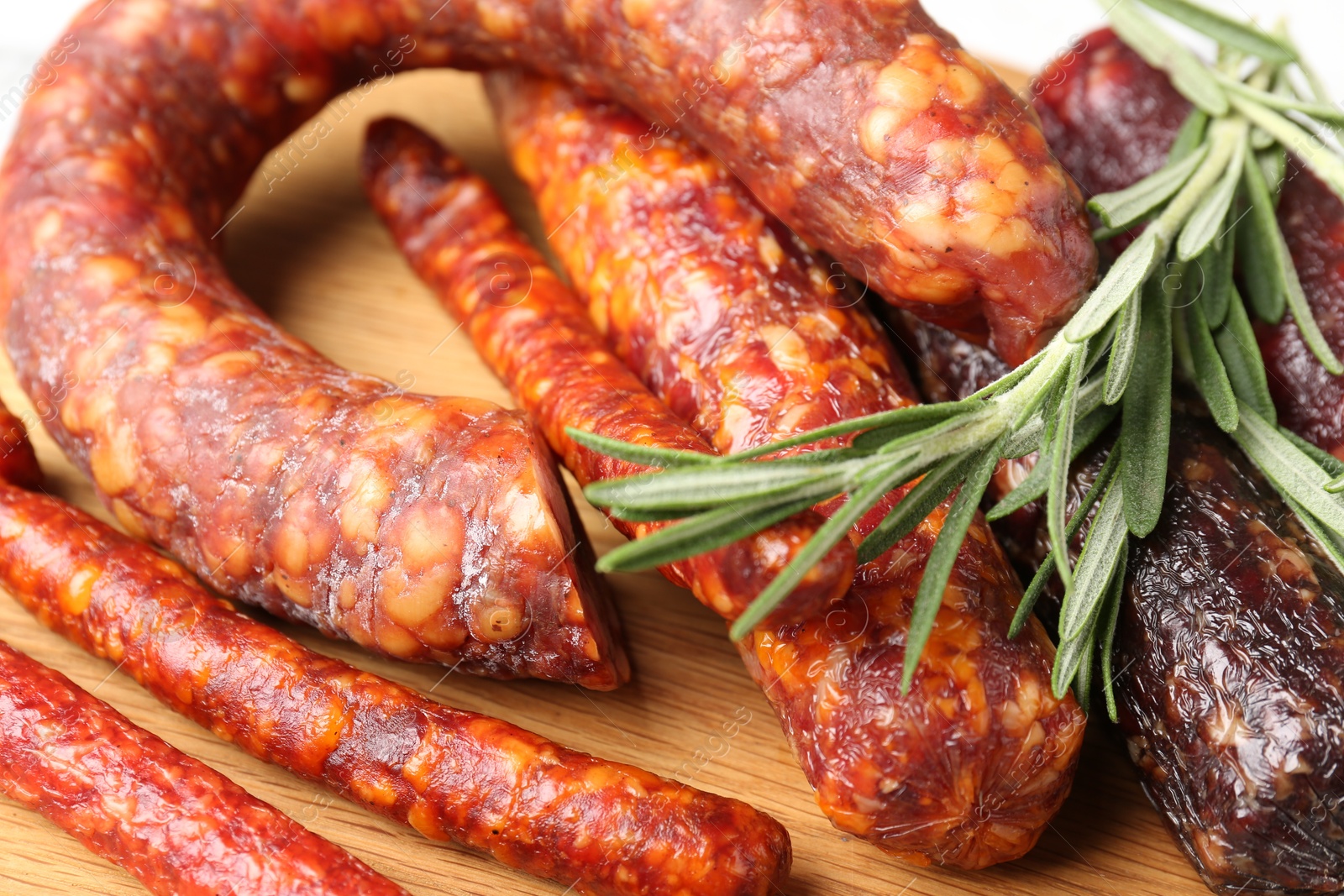 Photo of Different smoked sausages and rosemary on wooden board, closeup