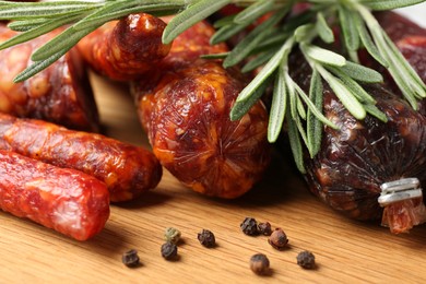 Photo of Different smoked sausages, rosemary and peppercorns on wooden board, closeup